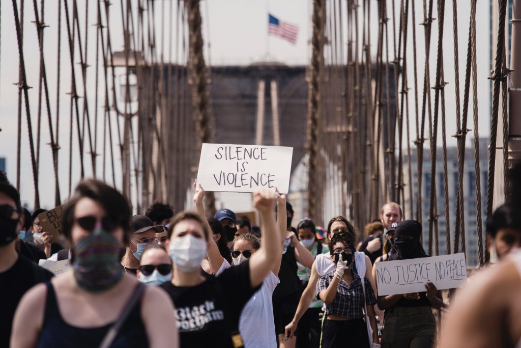 White person at a rally for social justice holding a sign that says "silence is violence".